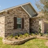 Side view of a newly built brick home with landscaped yard and wooden privacy gate at Alterra Sierra Vista in Rosharon, TX