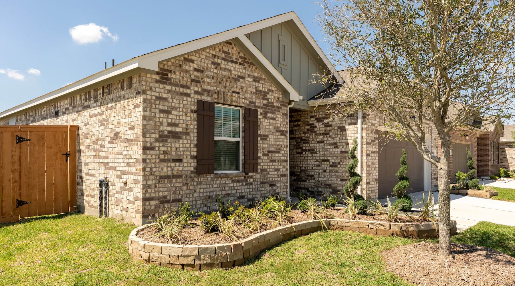 Side view of a newly built brick home with landscaped yard and wooden privacy gate at Alterra Sierra Vista in Rosharon, TX