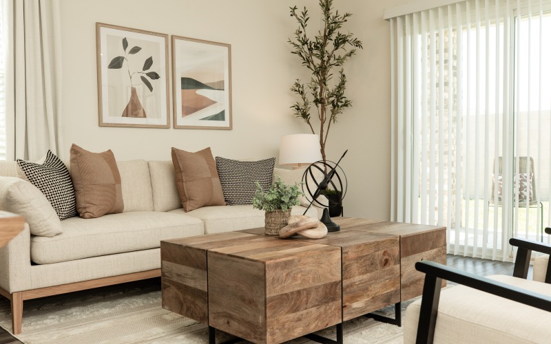 Bright and modern living room in a new home at Alterra Sierra Vista, featuring a cozy sofa, wooden coffee table, and natural light from large windows.